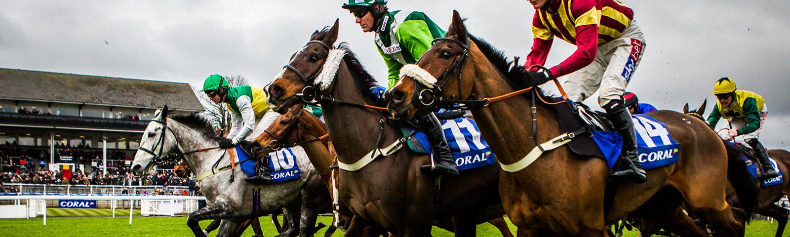 Four horses and jockeys racing past the grandstand at Chepstow Racecourse.