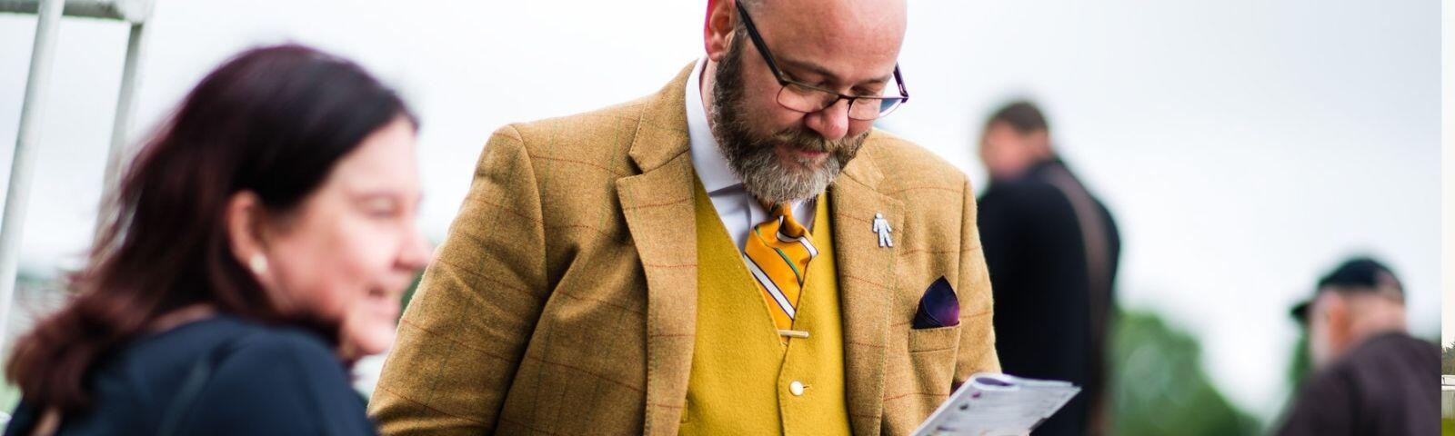 A well dressed man looks at a racecard